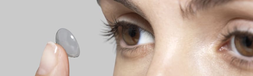 Close-up of a person holding a soft contact lens on their fingertip, aligned with brown eye, showing how to put contacts in correctly